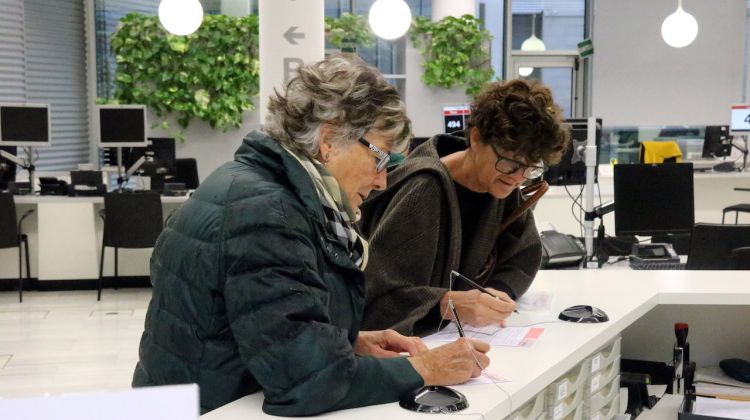 Pla mitjà de dues dones omplint un dels formularis abans de registrar la petició. ACN