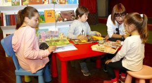 Imatge de tres infants i una mare asseguts a una taula de lectura (arxiu)