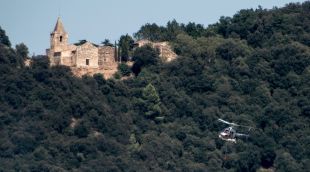 L'helicòpter bombarder dels Bombers treballant l'incendi amb la muntanya dels Sants Metges de fons