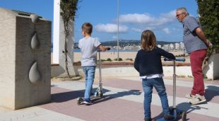 Pla mitjà de dos nens amb patinets amb el seu avi al Passeig de Palamós