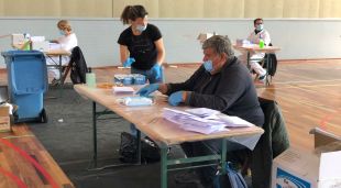 Un voluntari ensobrant les mascaretes que regala l'Ajuntament de Sant Feliu de Guíxols mentre una treballadora recull tots els sobres preparats per repartir