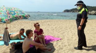 Una agent cívic a la platja del Canadell de Calella de Palafrugell informant uns banyistes de les mesures de seguretat