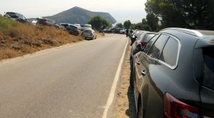 La carretera que baixa cap a Cala Montjoi amb cotxes aparcats a banda i banda