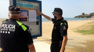 Agents de la Policia Local enganxant el ban que prohibeix l'accés a les platges de matinada