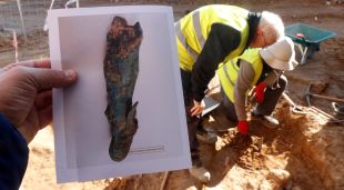 En primer terme, el fragment d'estàtua del déu Mercuri; al fons, els arqueòlegs excavant la necròpolis medieval