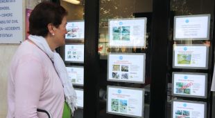 Una dona revisa les ofertes de pisos a la venda fora d'una immobiliària