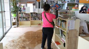 Una de les professores col·locant uns llibres en una prestatgeria amb el terra encara moll