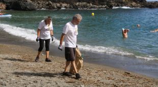 Dues persones recollint deixalles de la platja del Cau del Llop a Llançà