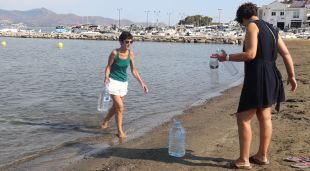 Dues dones omplen ampolles i garrafes del mar a la platja del Port de la Selva