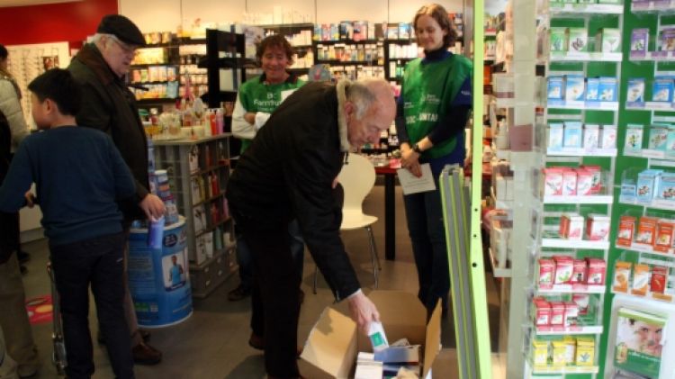 Dos ciutadans posant els medicaments que han comprat a la capsa dels voluntaris en una farmàcia de Girona © ACN