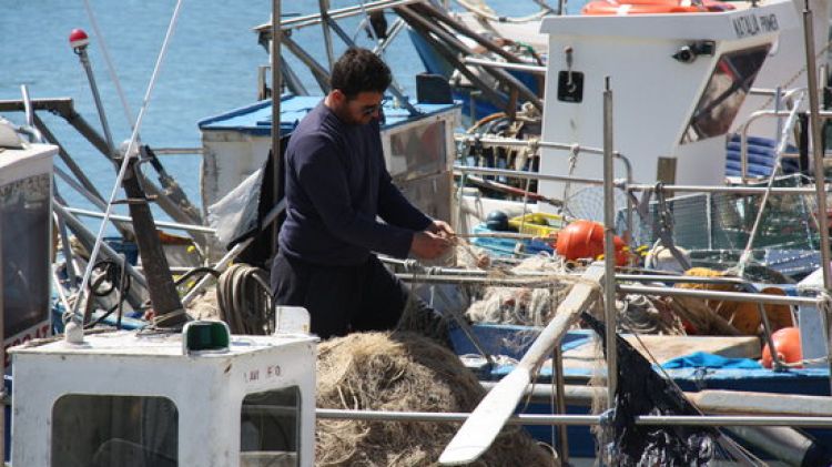Un pescador arreglant i recollint una xarxa al port de Roses © ACN
