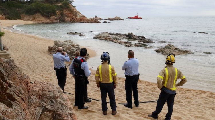 En primer terme, Bombers i Mossos d'Esquadra a la platja de Sa Conca i, al fons, l'embarcació de Salvament Marítim © ACN