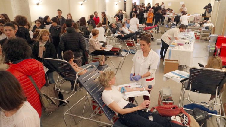 Ina donant fent-se les proves i a l'esquerra la cua de gent a la sala d'acte de l'escola Vedruna de Girona © ACN