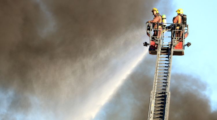Dos bombers amb les flames que afecten la planta de reciclatge de Sant Feliu de Buixalleu © ACN