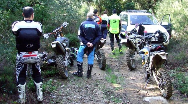 Els joves denunciats, d'esquenes, enmig d'un paratge natural amb les motos d'enduro