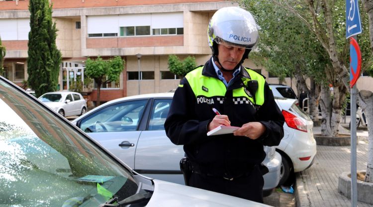 Un agent de la Policia Municipal multant un vehicle aparcat en una zona de minusvàlids (arxiu). ACN