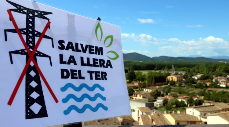 En primer terme, un cartell amb el nom de la plataforma; i al fons, el territori que queda afectat per la nova línia de 220 kV. ACN