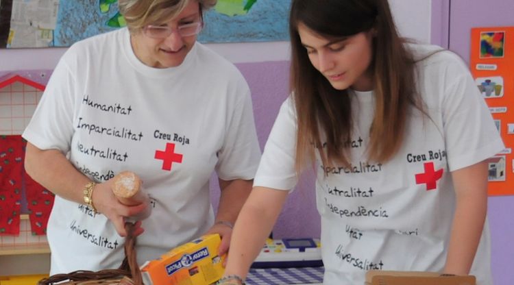 Dues voluntàries de la Creu Roja oferint aliments a nens amb risc d'exclusió social