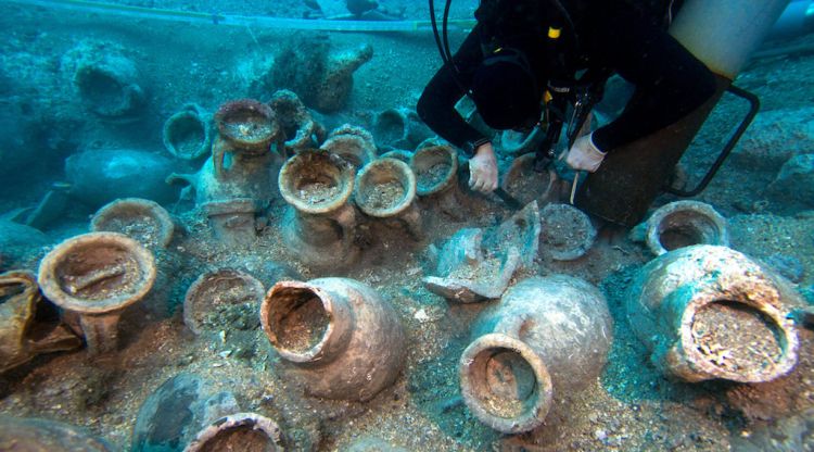 Un arqueòleg al costat d'algunes de les 135 àmfores descobertes al jaciment a tocar de les illes Formigues. ACN