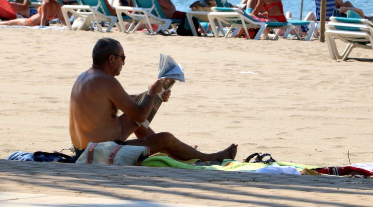 Un home llegint a l'ombra de la platja de Roses per combatre la calor aquest matí. ACN