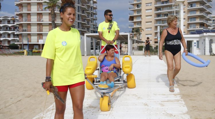 Dos socorristes de la platja de Torre Valentina ajuden a la Laura a entrar a l'aigua amb una cadira amfíbia. ACN