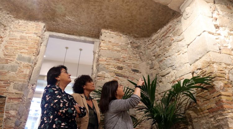 L'arqueòloga i les dues propietàries de l'òptica, mirant el pany de muralla medieval. ACN
