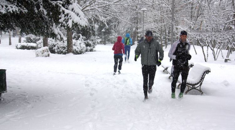 Diverses persones corrent per l'entorn de l'estany de Puigcerdà, cobert de blanc per la nevada. ACN