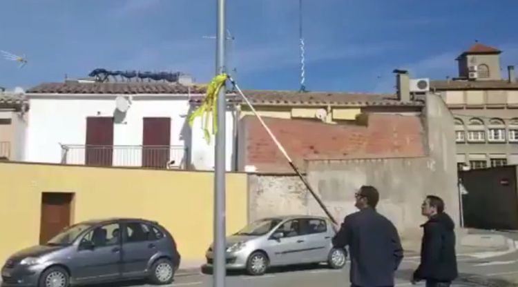 Pla obert de dos homes arrencant un llaç groc a la Bisbal