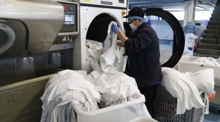 Una treballadora traient la roba d'una rentadora per col·locar-la en un cossi gran. ACN