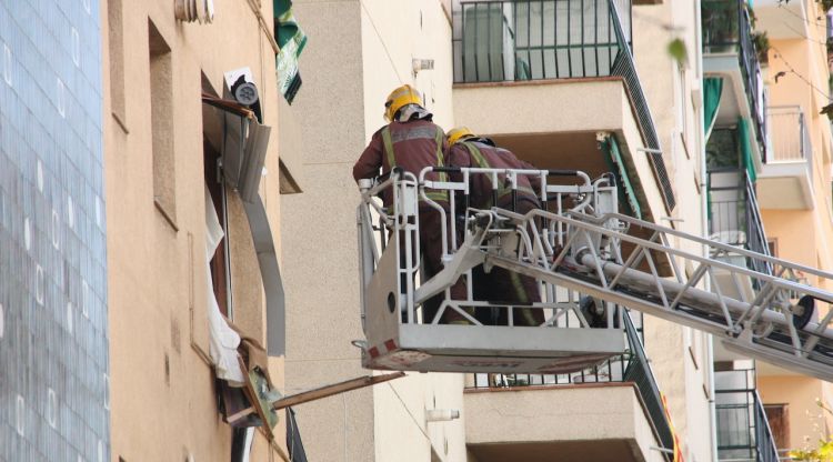 Dos bombers dalt d'una grua elevadora davant una finestra destrossada del pis sinistrat a Premià de Mar