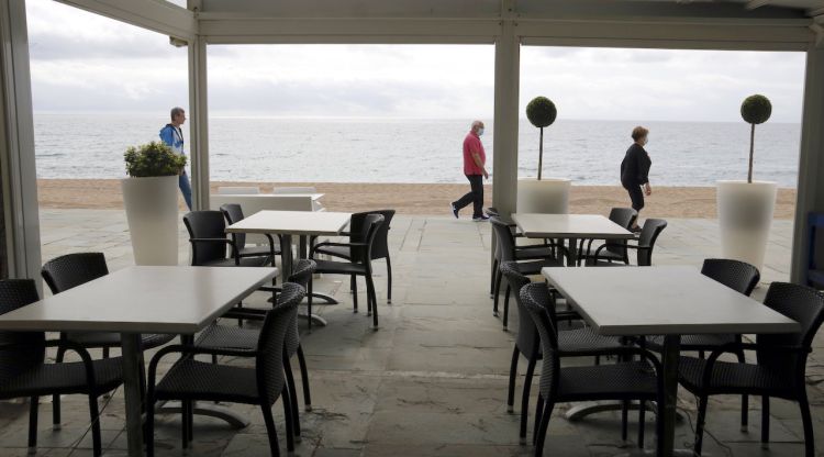 Una terrassa del passeig marítim de Platja d'Aro tancada i veïns passejant. ACN