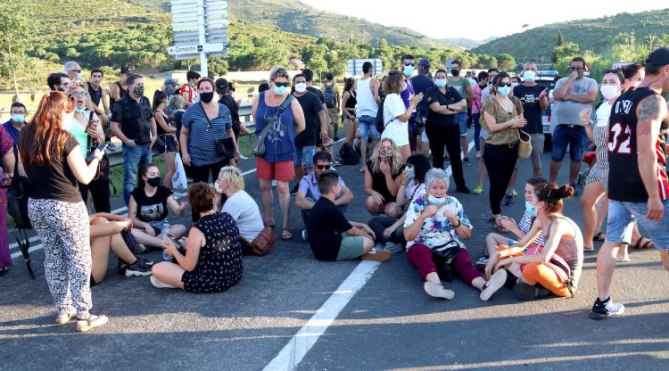 Els manifestants tallant l'N-260 a l'entrada de Llançà, alguns drets i alguns asseguts al terra. ACN