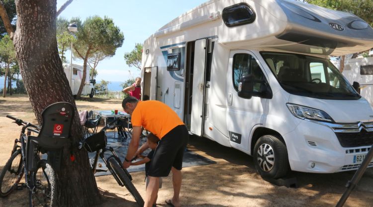 Pla curt d'un usuari arreglant la bicicleta al costat de l'autocaravana al Càmping Palamós (arxiu)