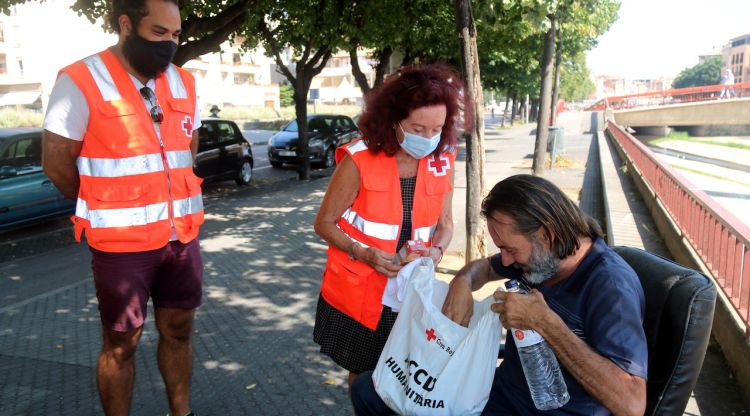 Voluntaris de la Creu Roja de Girona repartint un dels lots per combatre la calor i prevenir el coronavirus a un sensesostre. ACN