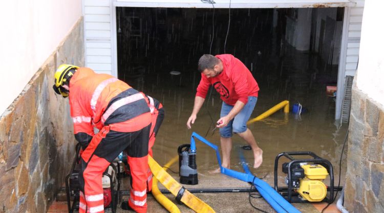 Dos bombers posant en marxa una bomba d'aigua amb el propietari d'un garatge inundat. ACN