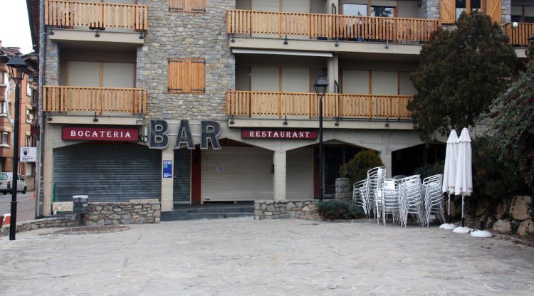 Pla obert on es veu un bar del centre d'Alp (Cerdanya) tancat i amb les taules de la terrassa recollides. ACN