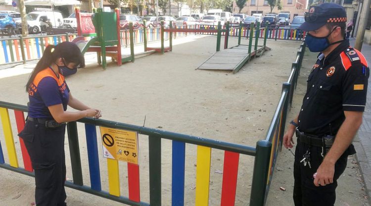 Dos voluntaris de Protecció Civil de Salt posant una cinta en un parc infantil per evitar que els infants hi accedeixin