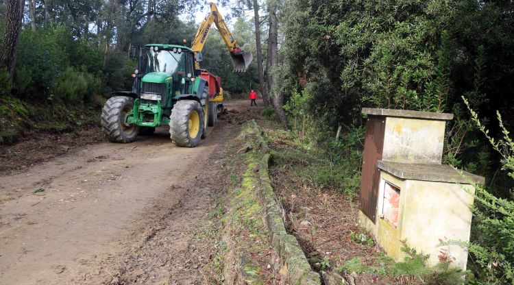 En primer terme, restes de voreres i una de les casetes d'obra; al fons, l'excavadora retirant els vestigis de formigó de l'antiga urbanització. ACN