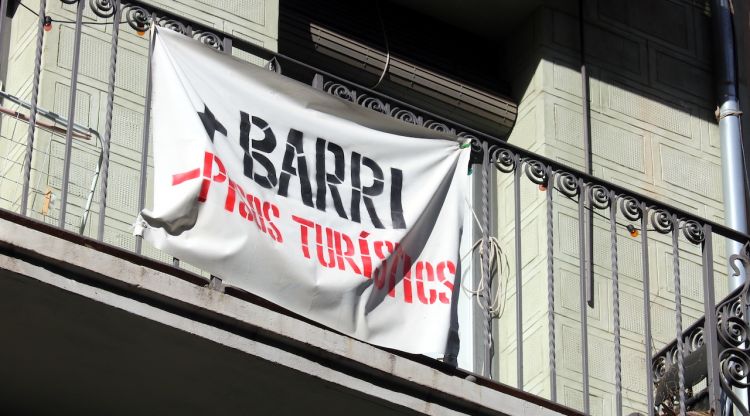 Un balcó a la Rambla de Girona amb el cartell '+Barri -Pisos Turístics'. ACN
