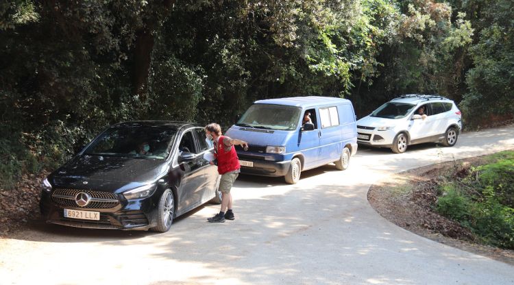 Tres cotxes que volen accedir a l'aparcament habilitat per anar a les gorgues de Sadernes mentre un informador explica el nou sistema de reserves. ACN