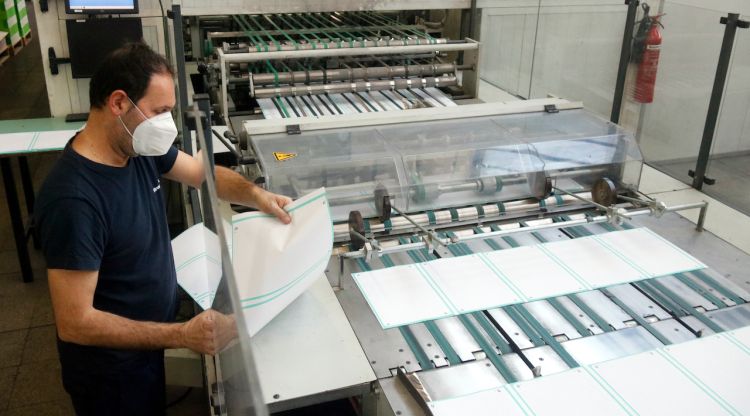 Un treballador supervisant el paper que surt d'una de les màquines i que després es convertirà en llibretes. ACN