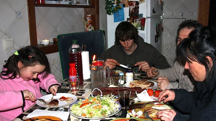 La família Solà Canaletes sopant la carn a la brasa que han cuinat a la llar de foc i amb la llum d'una espelma © ACN