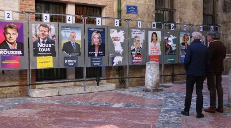Dos homes observant els cartells electorals que hi ha a tocar de l'Ajuntament de Perpinyà. ACN