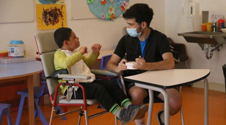 Un treballador li dona el dinar a un nen amb discapacitat en un centre de Sant Gregori, aquest matí. ACN