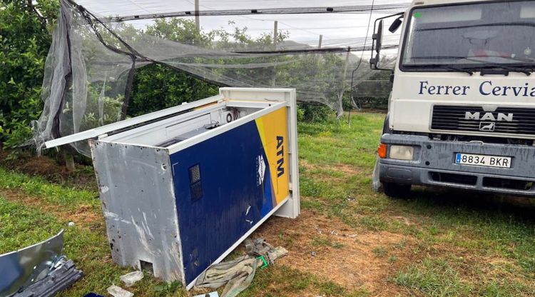 En primer terme, el caixer desmuntat a peces; al fons, el camió robat que els lladres han abandonat al camp de pomeres. ACN