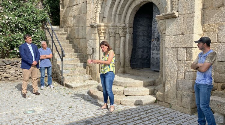 La guia de patrimoni Pilar Aláez explicant la portalada de l'església de Sant Esteve de Guils de Cerdanya on es veu al president de l'ens comarcal, Isidre Chia, escoltant la visita. ACN