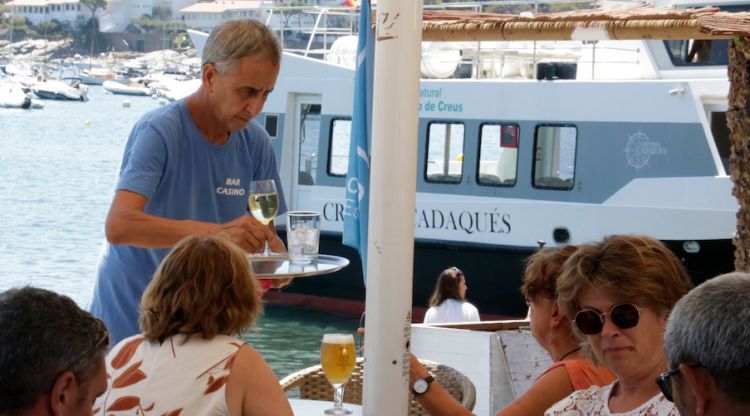 Un cambrer servint taules i, al fons, el mar a Cadaqués. ACN