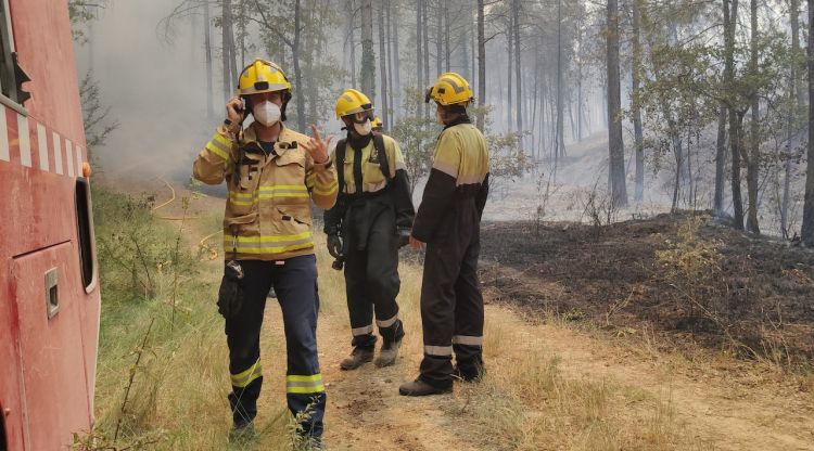 Un bomber saludant a càmera amb dos AOF al fons en un incendi forestal