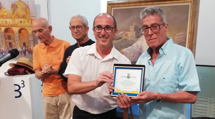 Albert Roca (dreta) rep, de mans de l'alcalde de Palamós, la placa de reconeixement durant l'acte d'homenatge a l'artista que va tenir lloc l'agost passat