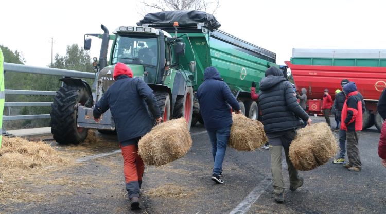 Un grup de pagesos portant bales de palla per obstaculitzar la via. ACN